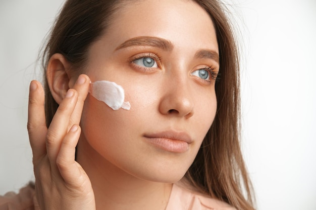 Photo close up portrait of a young blue eyes woman applying cream on face