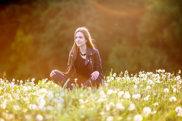 Close up portrait of young brunette girl with a necklace around his neck in dandelions on the sunset