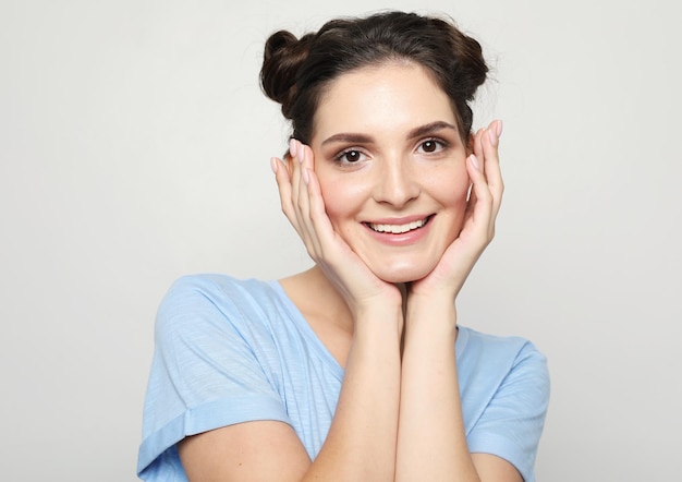 Close up portrait of young brunette woman in a blue tshirt posing on a light gray background