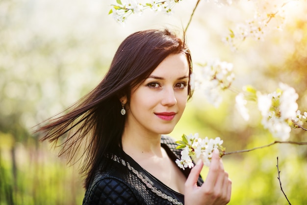 Photo close up portrait of young brunette woman with cherry blossom at spring garden.