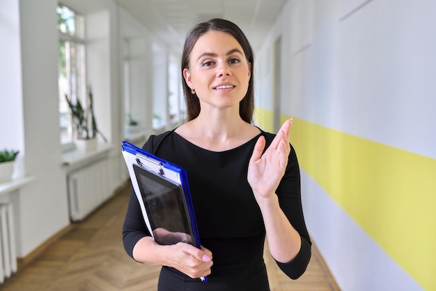 Photo close up portrait of young business woman talking and gesturing looking at camera inside office building. head shot of female teacher, psychologist, social worker in school corridor