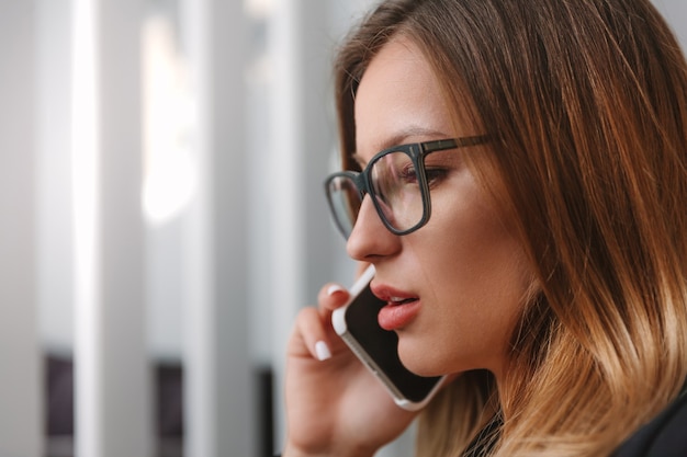 Close-up portrait of a young businesswoman in eyeglasses talking on a cell phone. Profile photo