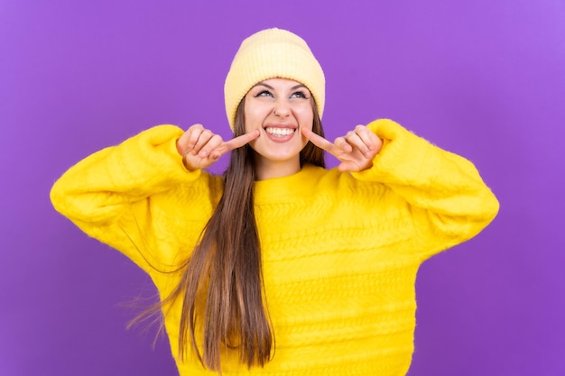 Close up portrait of a young cheerful woman isolated on purple studio background in yellow woolen pullover smiling