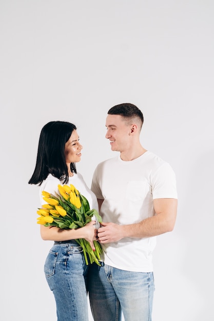 Close up portrait young couple with yellow flowers isolated on white background. lovely couple embracing with dreamy amorous expression. Celebrating valentine , woman's day.