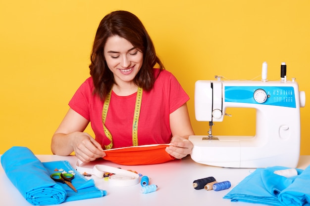 Close up portrait of young dressmaker woman sews clothes on sewing machine