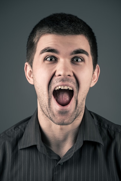 Close-up portrait of a young emotional cheerful brunet man on a gray background.