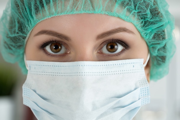 保護マスクと帽子をかぶった若い女性外科医の医師またはインターンのクローズアップの肖像画。ヘルスケア、医学教育、救急医療サービス、外科または獣医の概念
