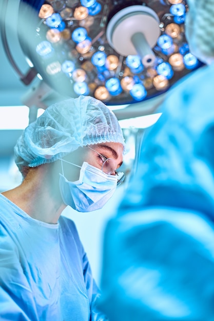 Close up portrait of young female surgeon doctor wearing protective mask and hat during the operation. Healthcare, medical education, surgery concept