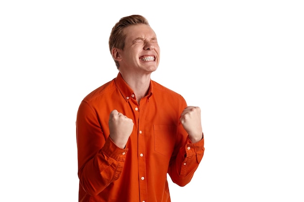 Close-up portrait of a young goodly ginger man in a stylish orange shirt acting like he is overjoyed about something while posing isolated on white studio background. Human facial expressions. Sincere