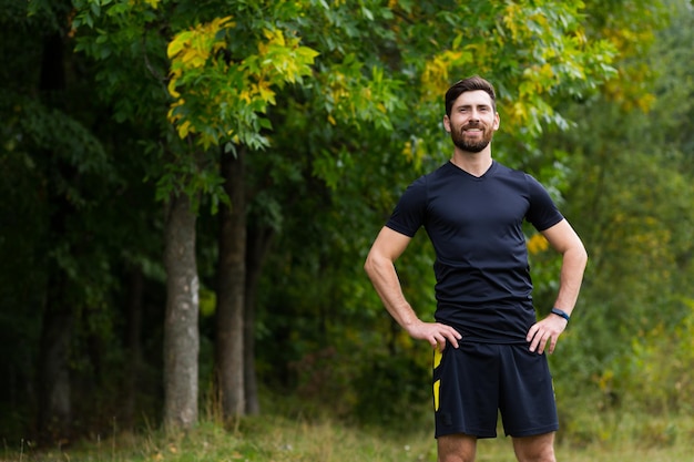 Close up portrait young happy bearded man standing in nature between forest trees relaxes, breathes fresh air closing his eyes. Male enjoys a life of peace calm, quiet in the park. Outdoors. Happiness