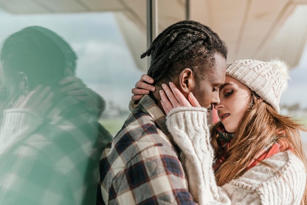 Photo close up portrait of a young interracial couple trying to kiss where woman is holding her boyfriend face in her hands close outside while dating