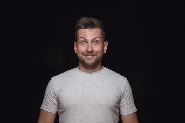 Close up portrait of young man isolated on black studio background. Photoshot of real emotions of male model. Wondering, exciting and astonished. Facial expression, human emotions concept.