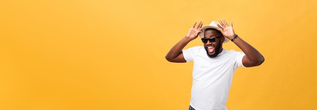 Close up portrait of a young man laughing with hands holding hat isolate over yellow background