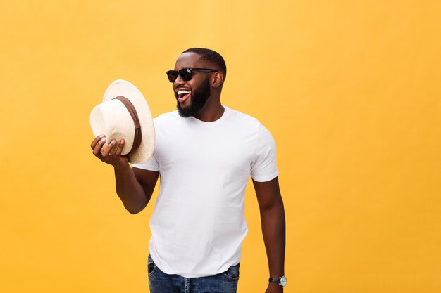 Close up portrait of a young man laughing with hands holding hat isolate over yellow background