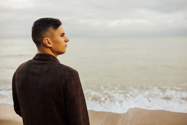 Close-up portrait of young man walking on beach towards water.