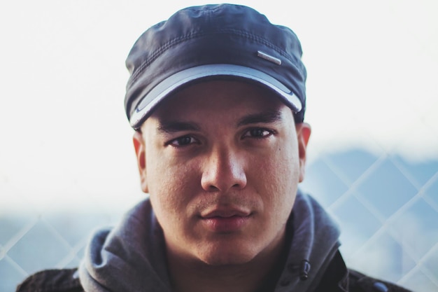 close-up portrait of young man wearing cap against fence