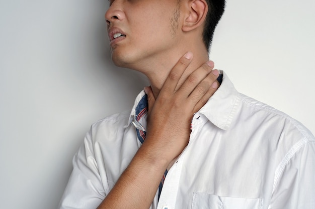 Foto primo piano ritratto di giovane uomo che indossa una maschera sanitaria che ha mal di gola e si tocca il collo