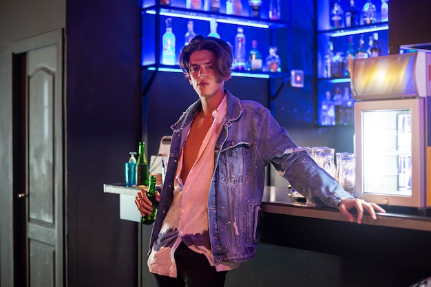 Close-up portrait of young man with a beer and jean jacket at the bar