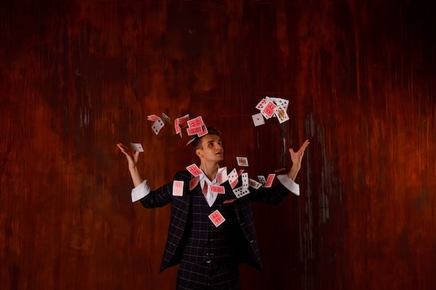 도박 카드와 함께 젊은 남자의 클로 우즈 업 초상화입니다. 잘생긴 남자는 카드로 트릭을 보여줍니다. 갈색 질감 배경에 마술사의 영리한 손입니다. 엔터테인먼트 및 취미의 개념입니다. 저작권 공간
