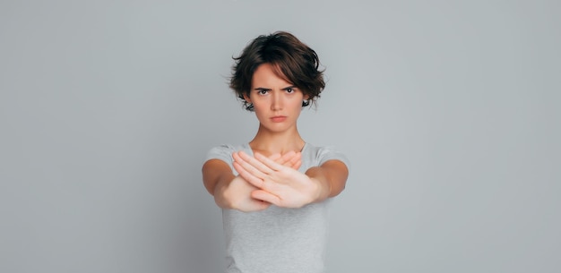 Close up portrait of young serious confident woman in casual clothes shows crossed palms no stop forbidden symbol or sign isolated on gray background