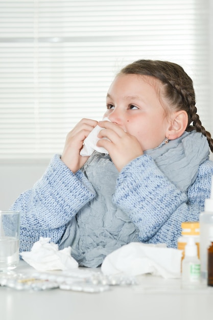 Close up portrait of young sick girl with medicines sitting at\
table