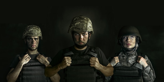 Закройте вверх по портрету молодых солдат. Мужчины и женщины в военной форме на войне на черной стене