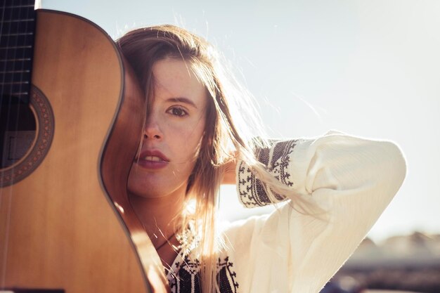 Foto ritratto in primo piano di una giovane donna con la chitarra contro un cielo limpido