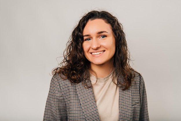 Close up portrait of young woman in casual looking at camera and smiling over grey background