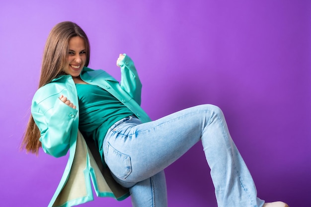 Close up portrait of a young woman cheerful or laughing isolated on purple studio background in blue windbreaker