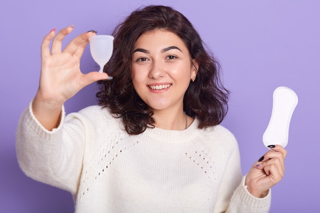 Chiuda sul ritratto della giovane donna che sceglie la tazza mestruale invece del tovagliolo sanitario