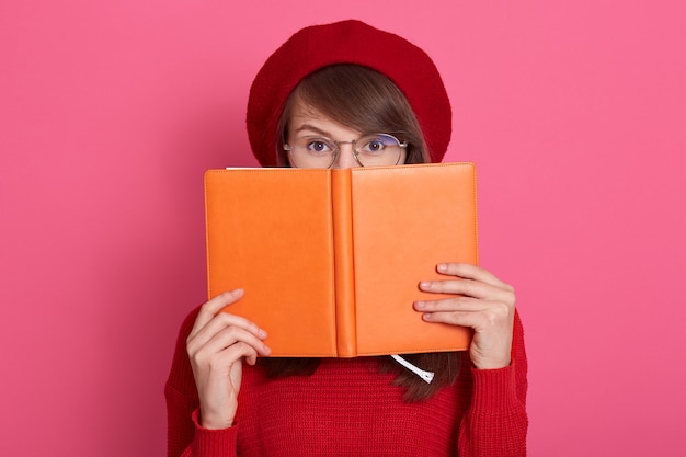 Close up portrait of young woman hides her face behind her notebook orange notebook