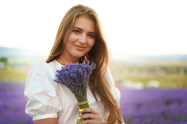 ラベンダー畑に立っている間、ラベンダーの花束を保持している若い女性の肖像画を間近します。