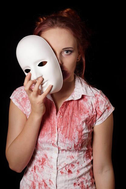 Close-up portrait of young woman holding mask over black background