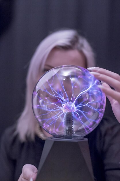 Close-up portrait of young woman holding plasma ball over black background