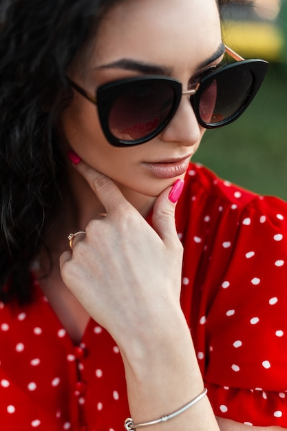 Foto ritratto del primo piano della giovane donna con gli occhiali da sole di modo in vestito rosso all'aperto