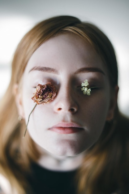 close-up portrait of young woman with flowers on eyes