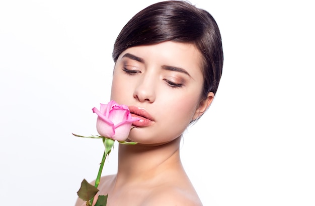 Close-up portrait of a young woman with natural makeup holding a pink rose.