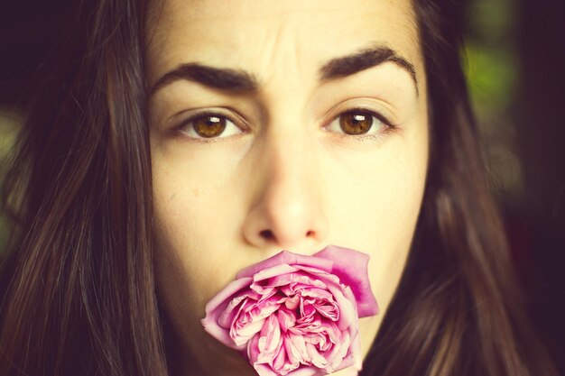 Foto ritratto in primo piano di una giovane donna con una rosa rosa in bocca