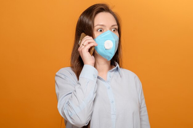 Close-up portrait of young woman on yellow orange wall in protective medical mask