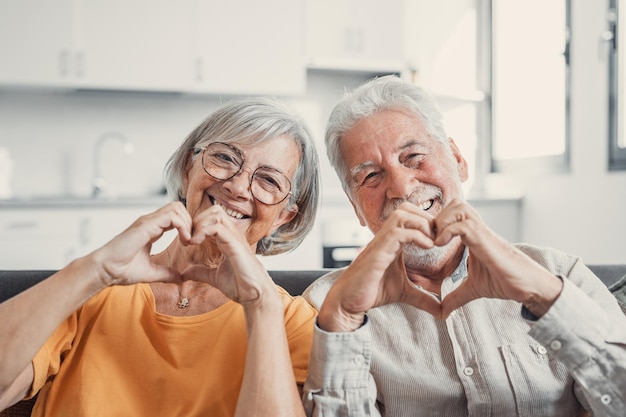 Close-up portret gelukkig oprechte bejaarde gepensioneerde familie paar hart gebaar maken met vingers liefde tonen of tonen van oprechte gevoelens samen binnenshuis kijken naar camera xA