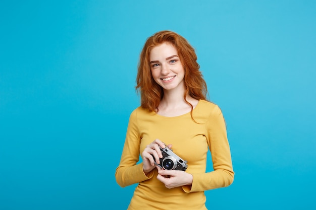 Close-up portret jonge mooie aantrekkelijke gember meisje gelukkig lachend met vintage camera en klaar om te reizen geïsoleerd op blauwe pastel muur kopie ruimte