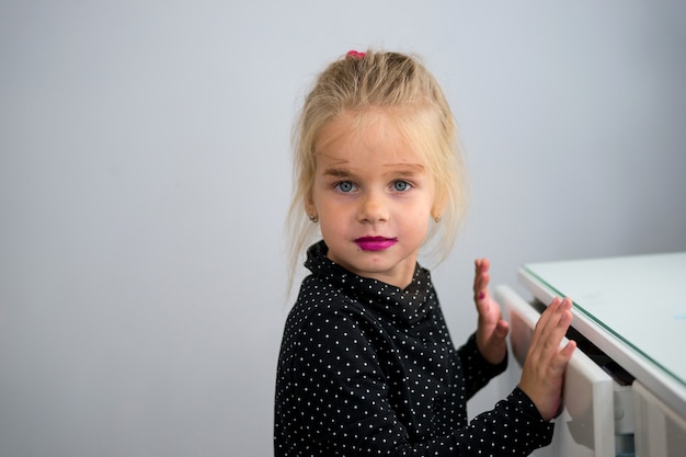 Close-up portret klein blond meisje maakte haar eigen make-up met de cosmetica van haar moeder