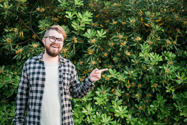 Close-up portret knappe jonge man wijst over groene struik buiten kopieerruimte en plaats voor reclame