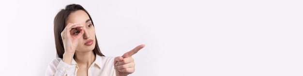 Close-up portret van aantrekkelijke eigenzinnige jonge vrouw die een verrekijker maakt met handen die ok gebaar op witte studio-achtergrond tonen