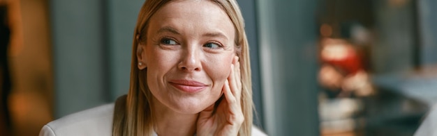 Close-up portret van aantrekkelijke glimlachende zakenvrouw in jas die in een café zit en naar de zijkant kijkt