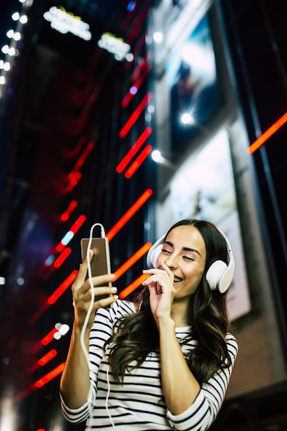 Close-up portret van aantrekkelijke jonge gelukkige vrouw in koptelefoon met slimme telefoon in handen buitenshuis