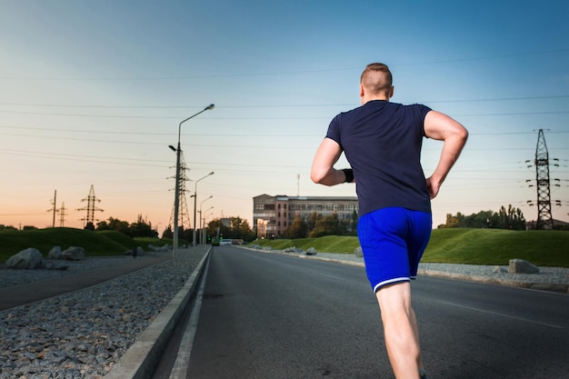 Close-up portret van atletische man die op de weg loopt, gespierde jonge hardloper die traint tijdens het joggen in het park. Avond. uitzicht vanaf de achterkant