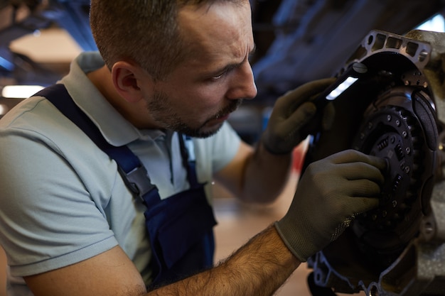 Close-up portret van bebaarde automonteur versnellingsbak in auto werkplaats repareren, kopie ruimte