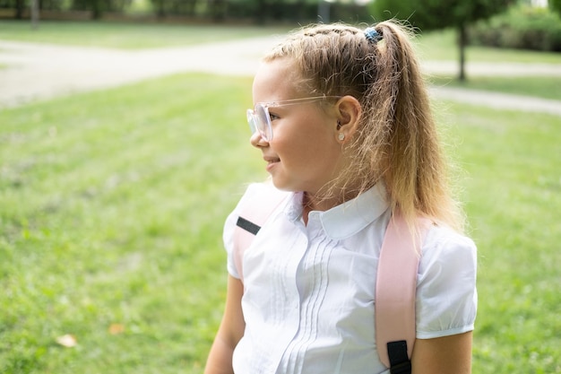 close-up portret van blond schoolmeisje in glazen wit overhemd met roze rugzak terug naar school