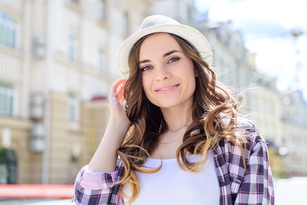 Close-up portret van charmante vrolijke ontspannen met rust chillen aantrekkelijke frisse zonnige dame met stralende brede glimlach lang krullend golvend bruin haar perfecte make-up, huizen gebouwen achtergrond